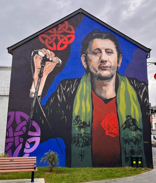 The Shane MacGowan mural at Emmet Place, Nenagh, by Neil O'Dwyer: Shane at a microphone in a green striped scarf with a red rose at his chest, against blue and black with Celtic knotwork